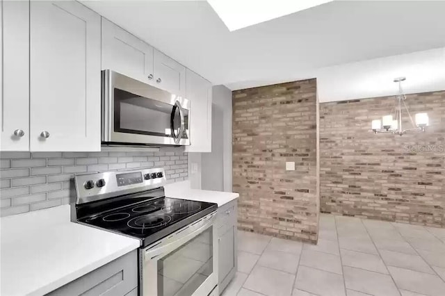 15609 Timberline Dr, Tampa, FL 33624 - kitchen featuring stainless steel appliances, light countertops, brick wall, a chandelier, and decorative backsplash