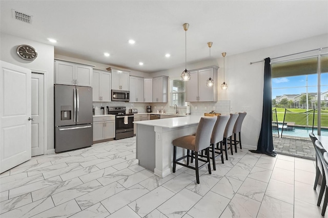 369 Ocean Course Ave, Davenport, FL 33896 - kitchen featuring appliances with stainless steel finishes, light marble finish flooring, a peninsula, a kitchen bar, and gray cabinets