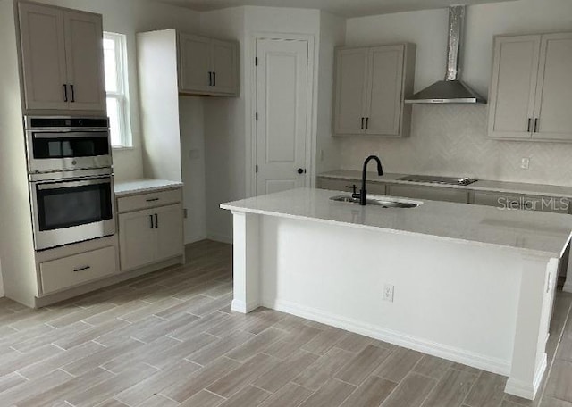 2971 Embark Trl, Saint Cloud, FL 34771 - kitchen with stainless steel double oven, light wood-type flooring, black electric stovetop, an island with sink, and backsplash