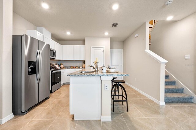 5645 Brosnan Rd, Saint Cloud, FL 34771 - kitchen featuring stainless steel appliances, white cabinets, light tile patterned floors, a breakfast bar area, and light stone countertops