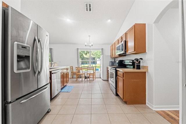 15364 Mount Sparrow Rd, Weeki Wachee, FL 34614 - kitchen featuring appliances with stainless steel finishes, brown cabinetry, a chandelier, lofted ceiling, and light countertops