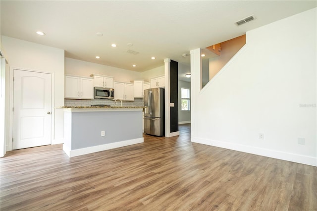 11081 Savannah Landing Cir, Orlando, FL 32832 - kitchen with appliances with stainless steel finishes, open floor plan, light wood finished floors, white cabinetry, and backsplash