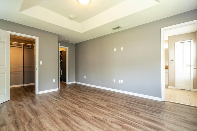 11081 Savannah Landing Cir, Orlando, FL 32832 - unfurnished bedroom featuring a walk in closet, wood finished floors, a closet, a tray ceiling, and connected bathroom