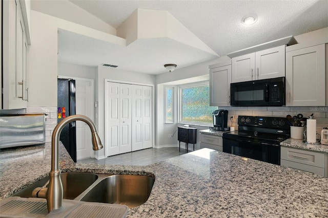 171 Cedarpark Ln, Davenport, FL 33837 - kitchen with black appliances, decorative backsplash, light stone countertops, wood finished floors, and vaulted ceiling
