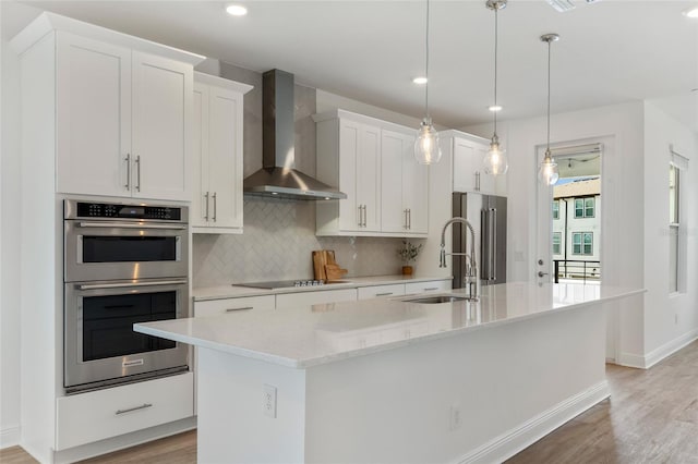 8484 Sperry St, Orlando, FL 32827 - kitchen with wall chimney exhaust hood, stainless steel appliances, light wood finished floors, a center island with sink, and white cabinetry
