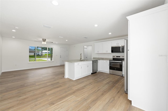13031 NE 7th Loop, Silver Springs, FL 34488 - kitchen featuring appliances with stainless steel finishes, a peninsula, open floor plan, white cabinetry, and light wood-style floors
