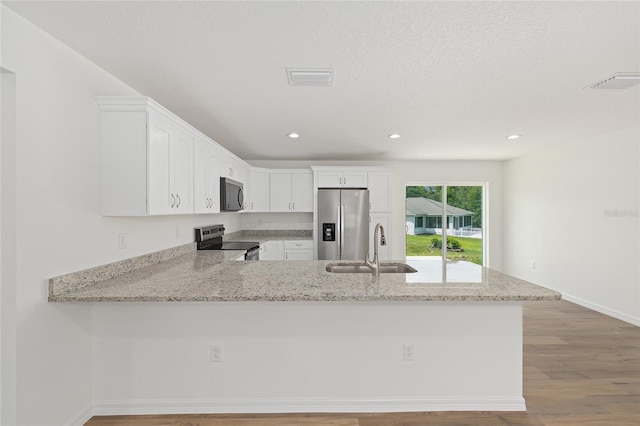 13031 NE 7th Loop, Silver Springs, FL 34488 - kitchen with appliances with stainless steel finishes, a peninsula, white cabinetry, light stone countertops, and wood finished floors