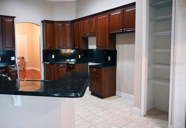 3504 Shorewood Dr, Kissimmee, FL 34746 - kitchen with decorative backsplash, arched walkways, dark brown cabinetry, and light tile patterned floors
