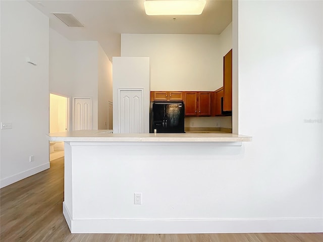2092 Switch Grass Cir, Ocoee, FL 34761 - kitchen with black fridge, a peninsula, light countertops, brown cabinetry, and light wood finished floors