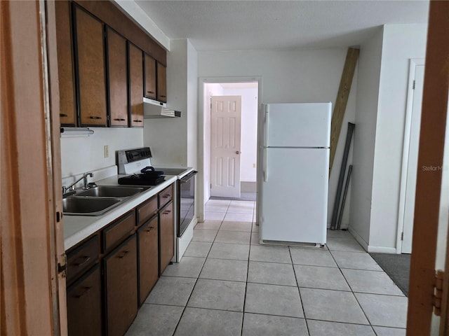 2308 18th St E, Bradenton, FL 34208 - kitchen with white appliances, under cabinet range hood, light countertops, light tile patterned floors, and dark brown cabinets