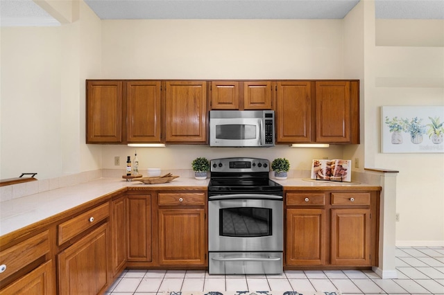 14558 Mandolin Dr, Orlando, FL 32837 - kitchen featuring stainless steel appliances, light countertops, light tile patterned flooring, and brown cabinets