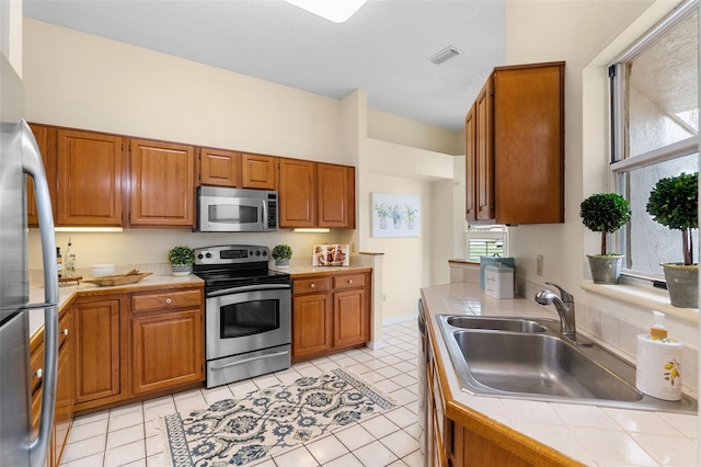 14558 Mandolin Dr, Orlando, FL 32837 - kitchen featuring appliances with stainless steel finishes, tile counters, and brown cabinets