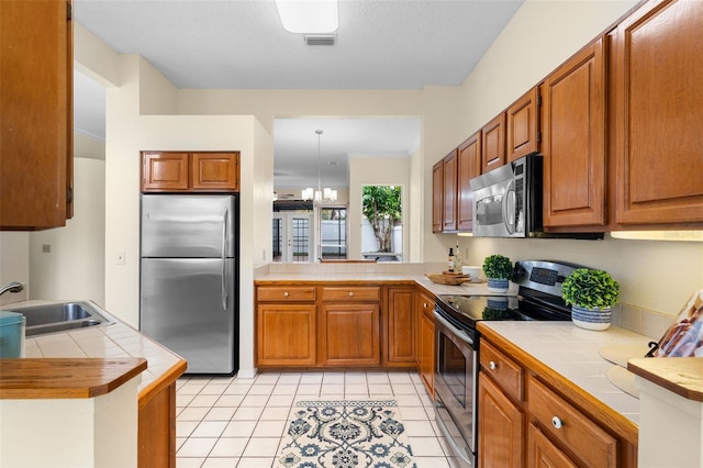 14558 Mandolin Dr, Orlando, FL 32837 - kitchen featuring stainless steel appliances, tile countertops, brown cabinetry, and light tile patterned floors