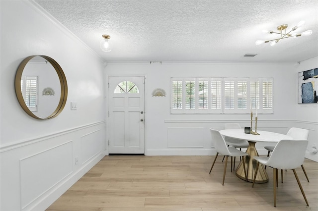 4611 Cranston Pl, Orlando, FL 32812 - dining room featuring a decorative wall, crown molding, a textured ceiling, light wood-style floors, and wainscoting