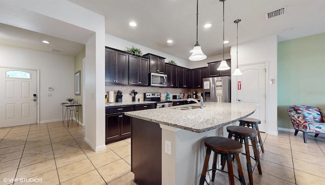 8806 Geneve Ct, Kissimmee, FL 34747 - kitchen featuring stainless steel appliances, light tile patterned floors, a breakfast bar area, dark brown cabinets, and a center island with sink