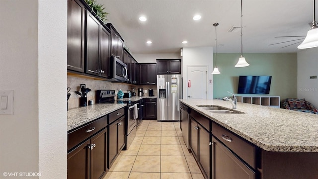 8806 Geneve Ct, Kissimmee, FL 34747 - kitchen with stainless steel appliances, a kitchen island with sink, dark brown cabinets, hanging light fixtures, and light tile patterned floors