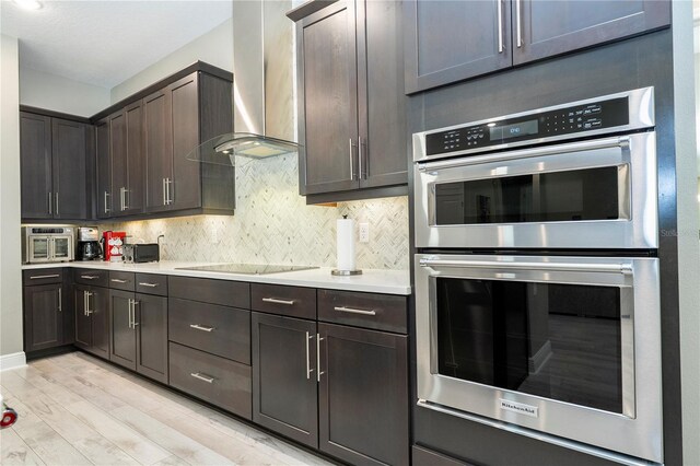 8066 Ludington Cir, Orlando, FL 32836 - kitchen featuring stainless steel double oven, wall chimney range hood, black electric cooktop, light wood-style floors, and dark brown cabinetry
