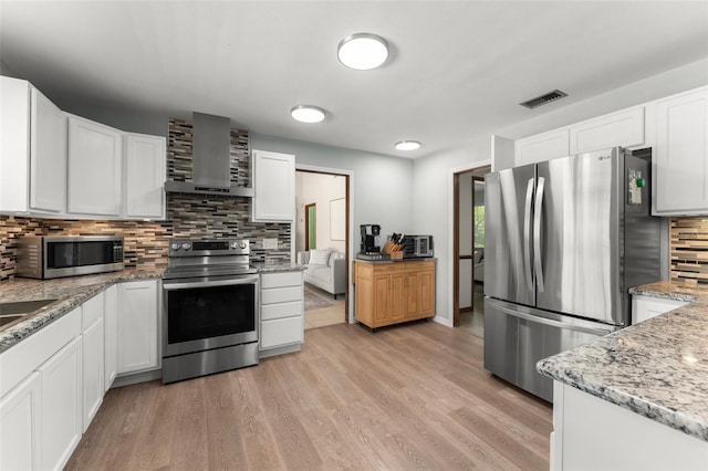 473 Burnt Tree Ln, Apopka, FL 32712 - kitchen with stainless steel appliances, wall chimney range hood, decorative backsplash, white cabinetry, and light wood-type flooring