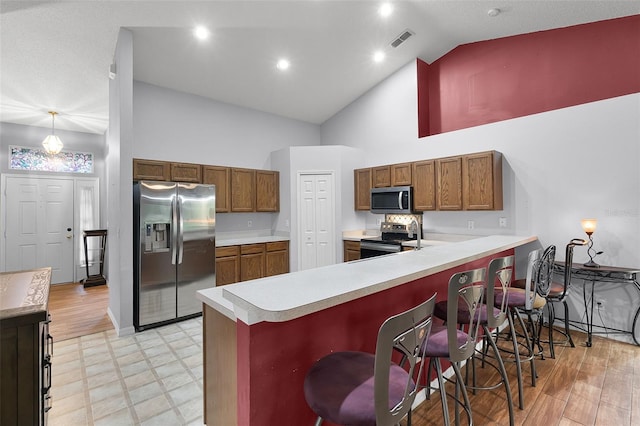 1113 Canopy Oaks Dr, Minneola, FL 34715 - kitchen featuring appliances with stainless steel finishes, high vaulted ceiling, light countertops, brown cabinets, and a peninsula