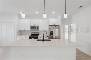 4572 SW 149th St, Ocala, FL 34473 - kitchen featuring stainless steel appliances, white cabinetry, a center island with sink, light countertops, and hanging light fixtures