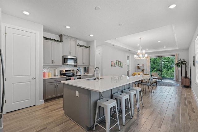 1388 Lombardi Ct, Kissimmee, FL 34759 - kitchen with stainless steel appliances, gray cabinetry, a raised ceiling, light wood-type flooring, and a breakfast bar area