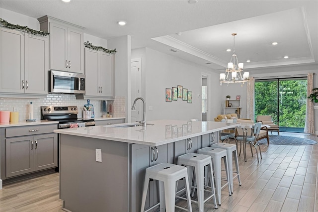 1388 Lombardi Ct, Kissimmee, FL 34759 - kitchen featuring appliances with stainless steel finishes, gray cabinetry, a tray ceiling, backsplash, and light wood-type flooring