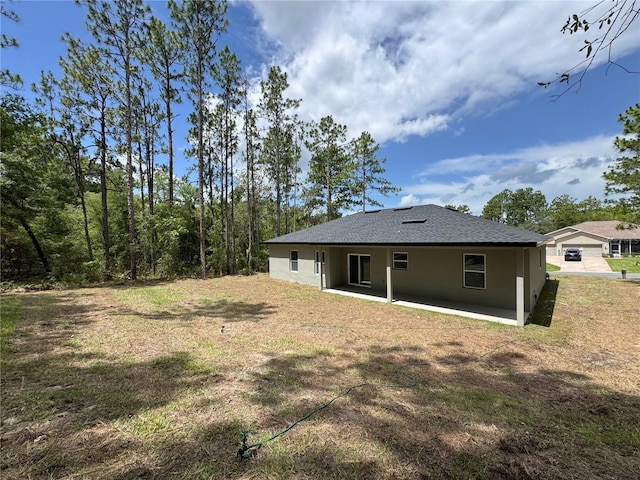 7687 N Quibble Ave, Dunnellon, FL 34434 - rear view of house with stucco siding, a patio, a shingled roof, and a lawn