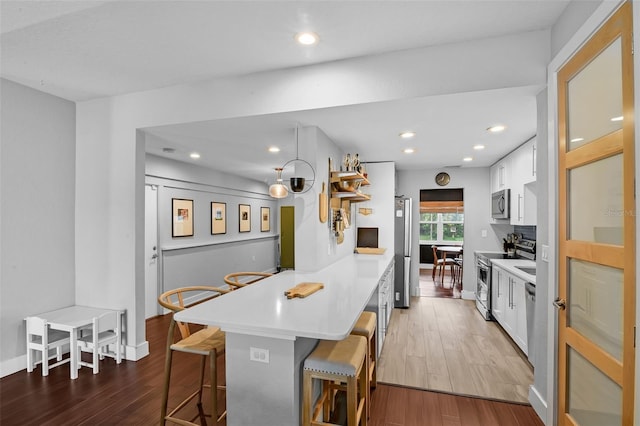 1322 N Bumby Ave, Orlando, FL 32803 - kitchen with stainless steel appliances, a breakfast bar area, a peninsula, light wood-style floors, and white cabinets