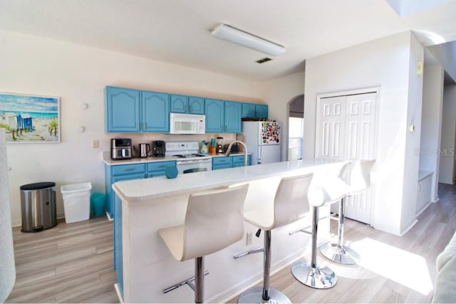 331 Bridgewater Dr, Davenport, FL 33897 - kitchen with white appliances, blue cabinets, light countertops, light wood-style floors, and a kitchen bar