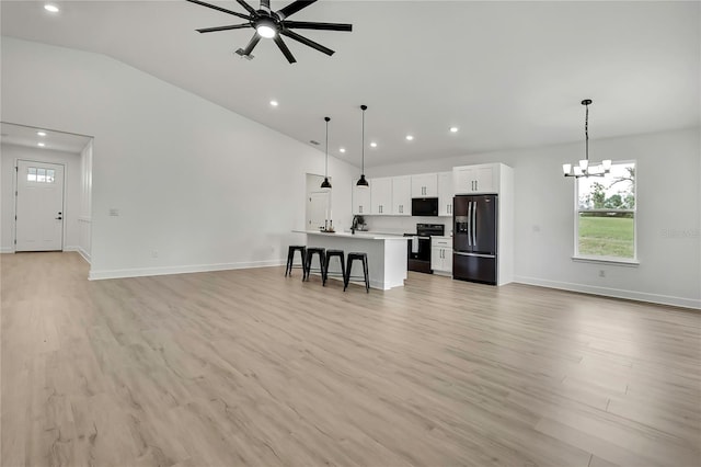 9739 Loretto St, Spring Hill, FL 34608 - unfurnished living room featuring vaulted ceiling, healthy amount of natural light, ceiling fan, a chandelier, and light wood-type flooring