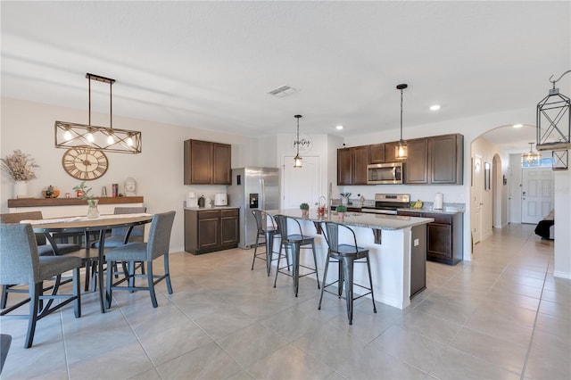 633 Greymount St, Davenport, FL 33837 - kitchen with stainless steel appliances, arched walkways, a breakfast bar area, an island with sink, and dark brown cabinetry