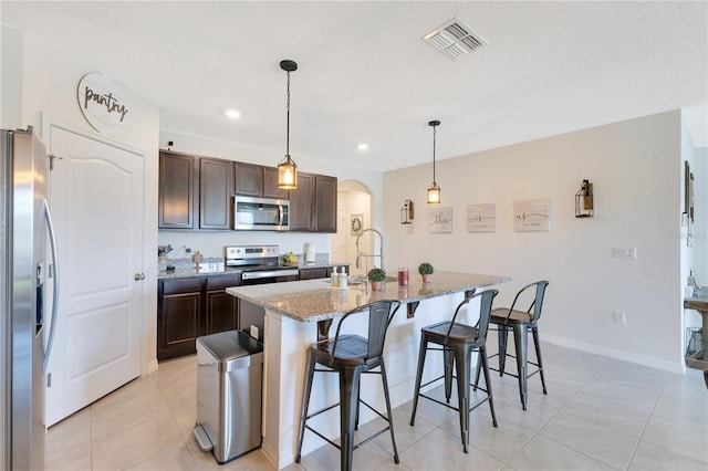 633 Greymount St, Davenport, FL 33837 - kitchen featuring appliances with stainless steel finishes, arched walkways, a breakfast bar area, dark brown cabinetry, and light tile patterned floors