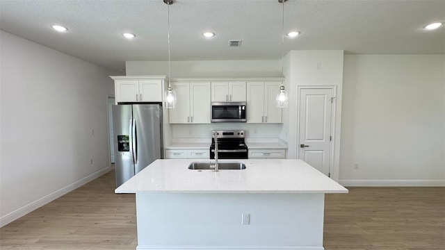 742 W Glenhaven Dr, Citrus Springs, FL 34434 - kitchen featuring appliances with stainless steel finishes, light wood-type flooring, white cabinetry, an island with sink, and hanging light fixtures