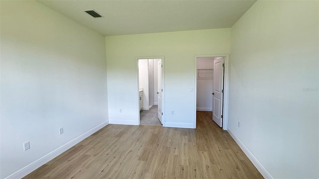 742 W Glenhaven Dr, Citrus Springs, FL 34434 - unfurnished bedroom featuring light wood-style floors, a spacious closet, a closet, and connected bathroom