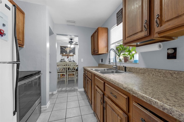 565 S Floyd Cir, Deltona, FL 32725 - kitchen featuring stainless steel electric range, freestanding refrigerator, brown cabinetry, light tile patterned floors, and ceiling fan