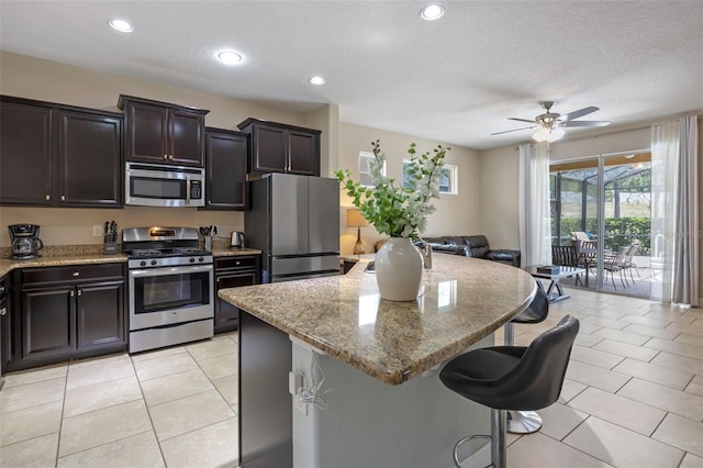 5172 Oakbourne Ave, Davenport, FL 33837 - kitchen featuring stainless steel appliances, a kitchen breakfast bar, a kitchen island, light tile patterned flooring, and a ceiling fan