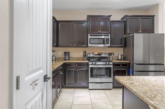 5172 Oakbourne Ave, Davenport, FL 33837 - kitchen featuring appliances with stainless steel finishes, light tile patterned floors, light stone countertops, and dark brown cabinetry