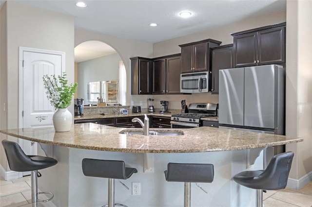 5172 Oakbourne Ave, Davenport, FL 33837 - kitchen featuring stainless steel appliances, arched walkways, light tile patterned floors, dark brown cabinets, and a kitchen bar