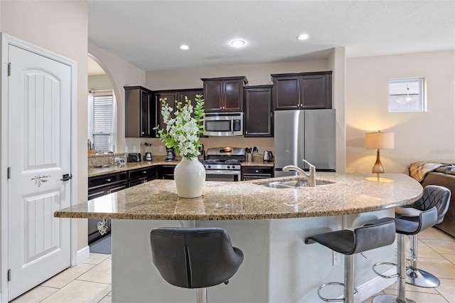 5172 Oakbourne Ave, Davenport, FL 33837 - kitchen with stainless steel appliances, a kitchen bar, light tile patterned floors, arched walkways, and light stone countertops