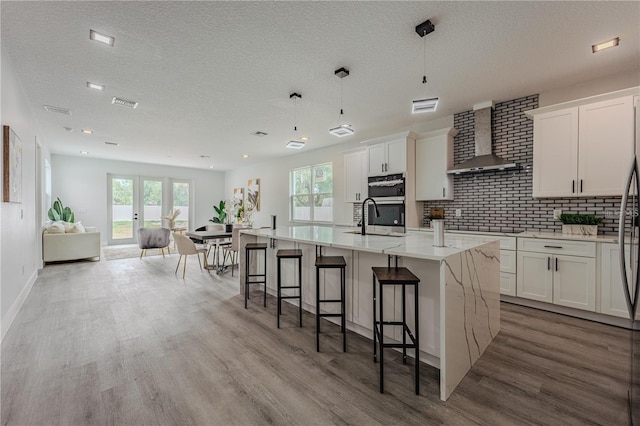 63 W 10th St, Apopka, FL 32703 - kitchen with wall chimney range hood, light wood-style floors, a center island with sink, a breakfast bar area, and backsplash