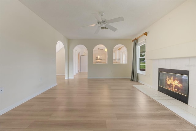 16243 Wilkinson Dr, Clermont, FL 34714 - unfurnished living room featuring light wood finished floors, a tile fireplace, ceiling fan, and arched walkways