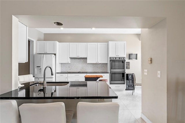 1225 Hollow Pine Dr, Oviedo, FL 32765 - kitchen with double oven, fridge with ice dispenser, decorative backsplash, white cabinets, and dark countertops