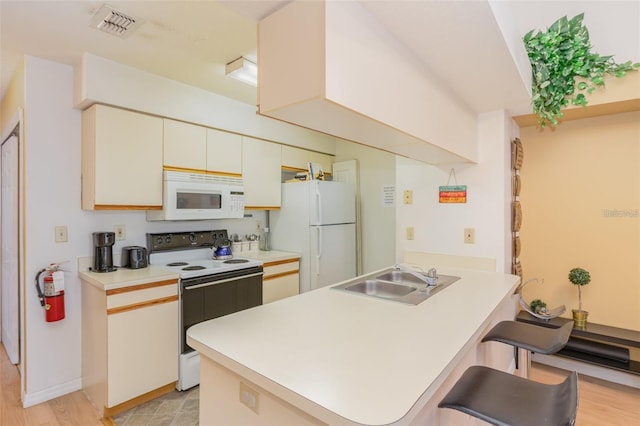 kitchen with white appliances, a peninsula, light countertops, and a breakfast bar area