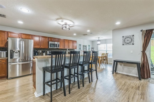 2032 Wavyleaf Ct, Apopka, FL 32712 - kitchen with appliances with stainless steel finishes, a textured ceiling, light wood finished floors, a breakfast bar, and recessed lighting