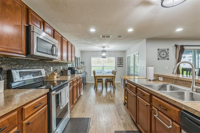 2032 Wavyleaf Ct, Apopka, FL 32712 - kitchen featuring appliances with stainless steel finishes, a textured ceiling, light wood finished floors, backsplash, and plenty of natural light