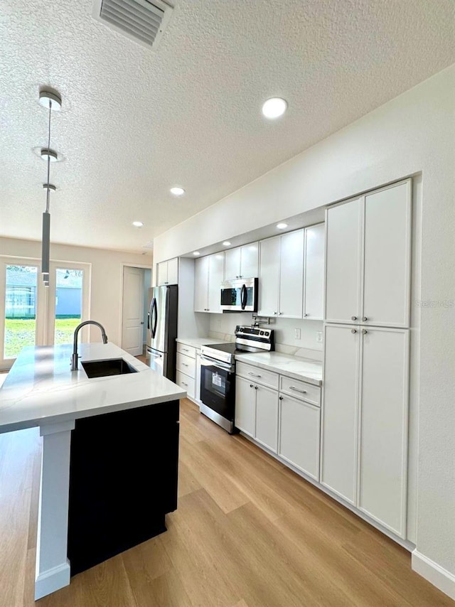 2634 De Groodt Rd SW, Palm Bay, FL 32908 - kitchen with stainless steel appliances, light wood finished floors, a textured ceiling, white cabinets, and light countertops