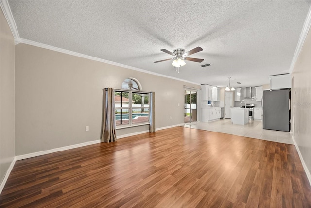 2725 White Magnolia Loop, Clermont, FL 34711 - unfurnished living room featuring a ceiling fan, light wood finished floors, ornamental molding, and a textured ceiling