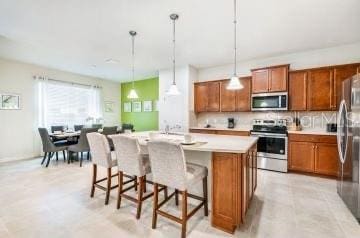 1512 Mumbai Way, Kissimmee, FL 34747 - kitchen featuring appliances with stainless steel finishes, brown cabinets, a kitchen island with sink, and a kitchen breakfast bar