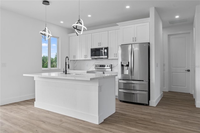10071 Kingsville Dr, Port Charlotte, FL 33981 - kitchen featuring appliances with stainless steel finishes, a kitchen island with sink, white cabinetry, wood finished floors, and recessed lighting