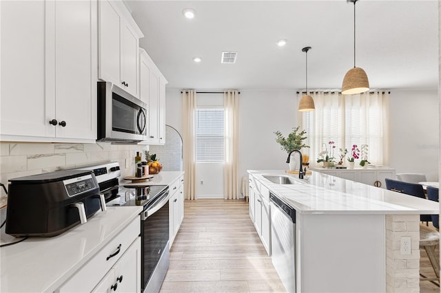 3279 Canna Lily Pl, Clermont, FL 34711 - kitchen featuring stainless steel appliances, light wood finished floors, a kitchen island with sink, tasteful backsplash, and white cabinets